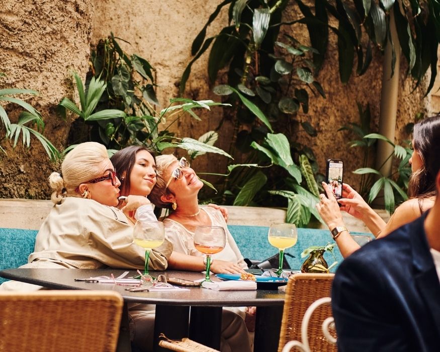 table with drinks and food, where three women are seated, engaged in conversation and laughter
