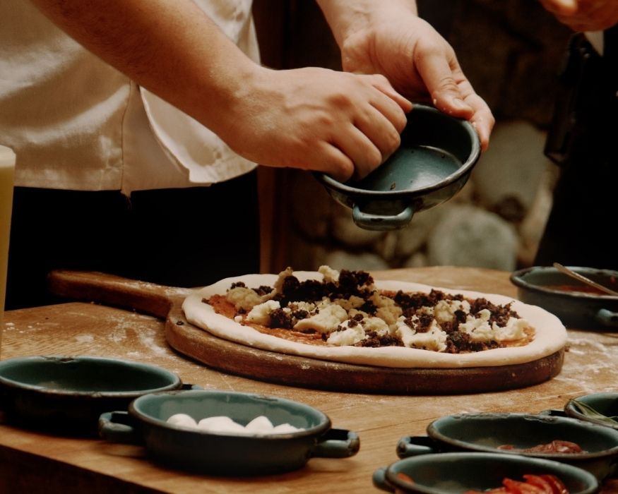 A man carefully places toppings on a pizza, showcasing his culinary skills in a bright kitchen setting