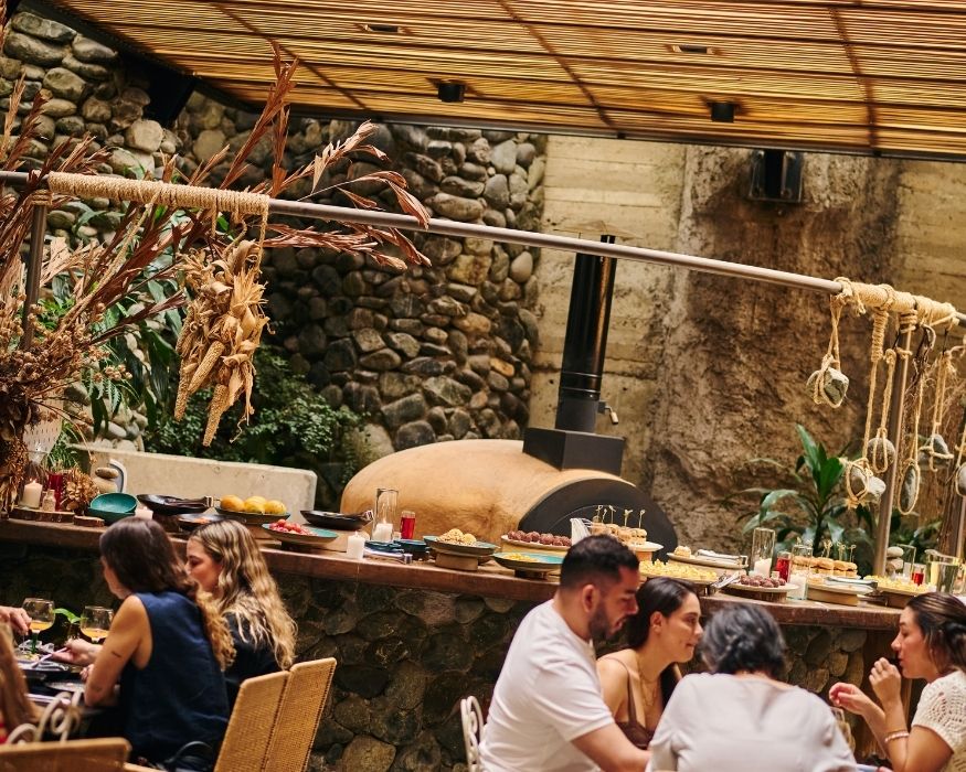 Guests seated at tables in a stone restaurant, sharing food and conversation in a charming setting.