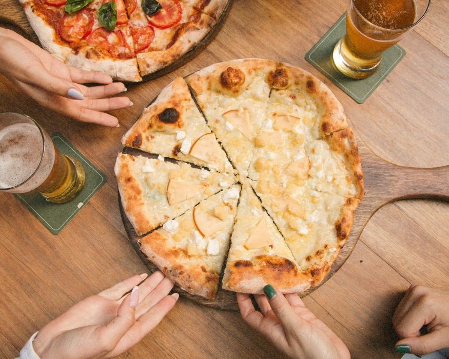 Several individuals gathered around a wooden table, each holding a slice of pizza, enjoying a shared meal together