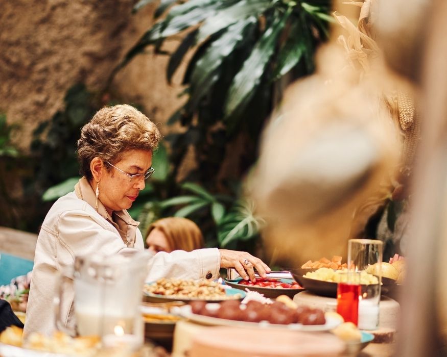 A woman is serving a selection of food at a buffet table, engaging with guests